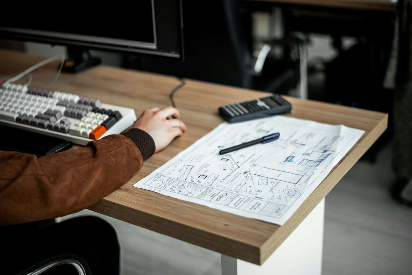 Designer working on architectural plans and UI wireframes at a desk.