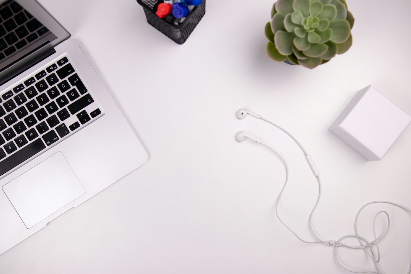 Organized white desk with a laptop, succulent, and pens.