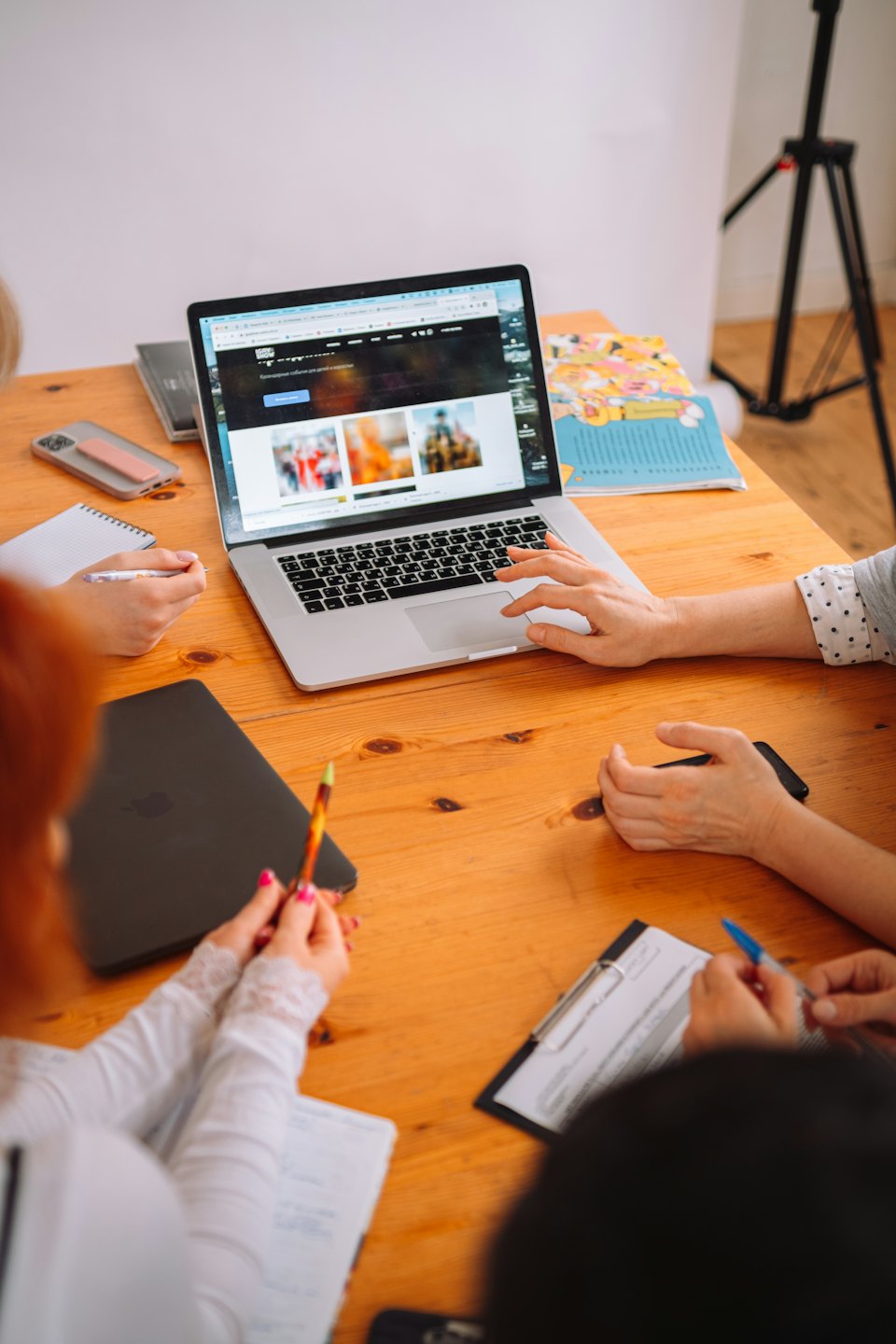 Team collaborates around a table with a laptop and notebooks.